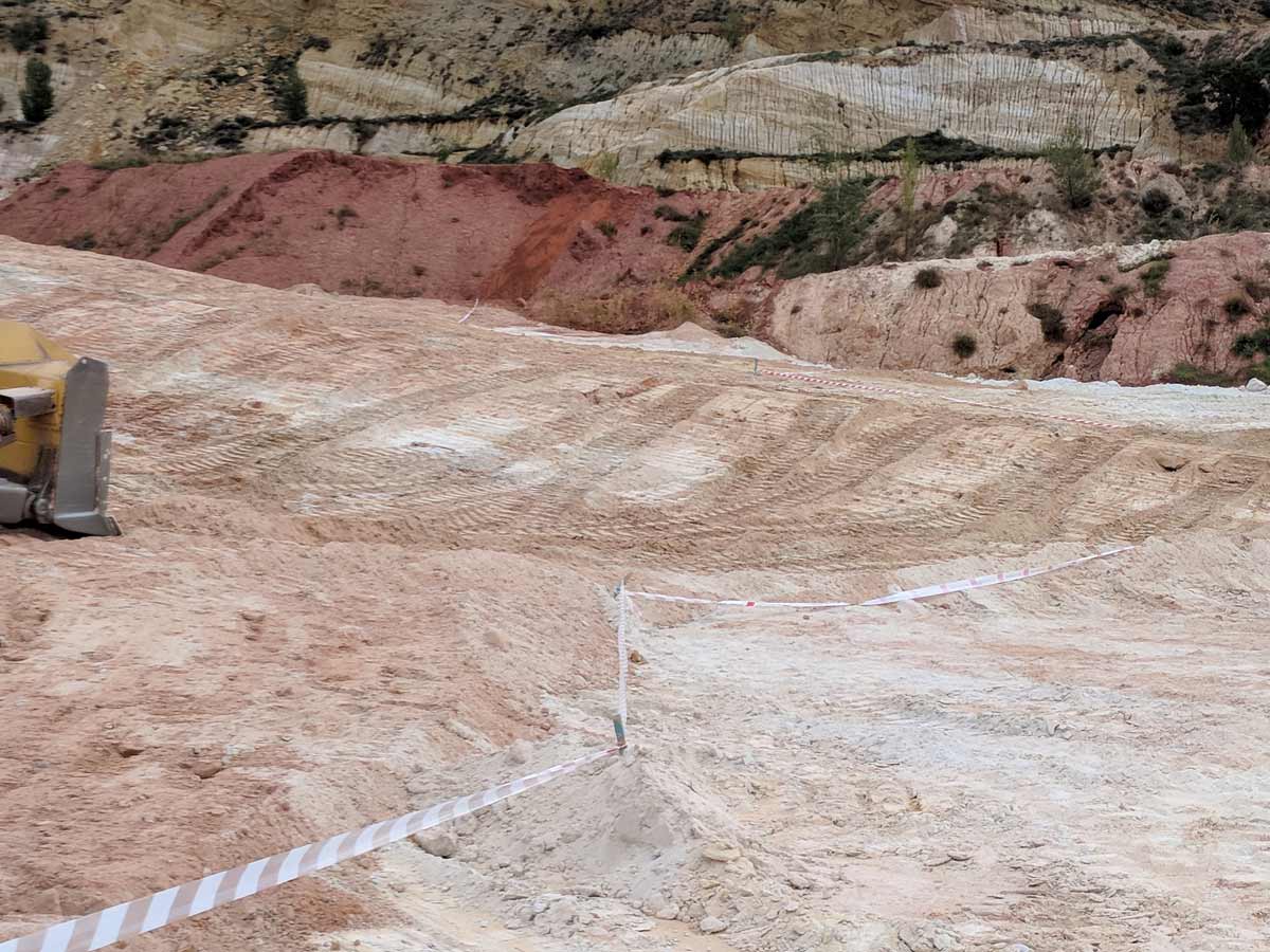 Construction site with earth-moving equipment and marked boundaries; terrain shows different soil layers.